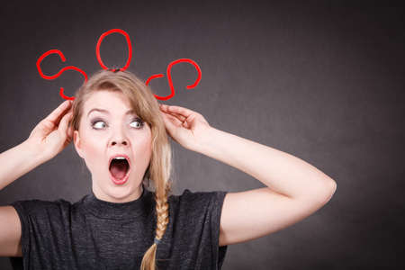 Fear and fright. Young blonde terrified woman needs help. Frightened hopeless female with red sos sign symbol on dark background.の写真素材