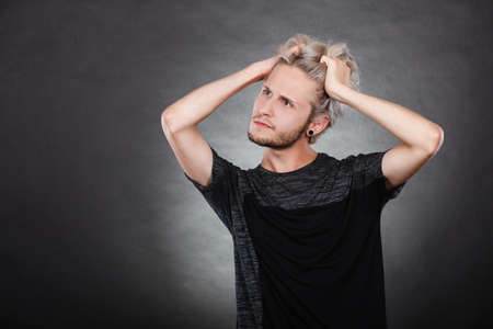 Young man confused thinking seeks a solution. Decision making process, doubt concept, studio shot on dark.の写真素材