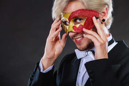Holidays, people and celebration concept. Elegant young guy wearing suit white shirt bow tie and carnival venetian mask, on dark.の写真素材
