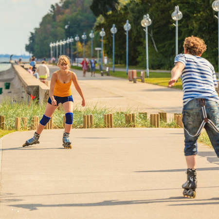 Holidays, active people and friendship concept. Young fit couple on roller skates riding outdoors on sea coast, woman and man rollerblading together on the promenadeの写真素材