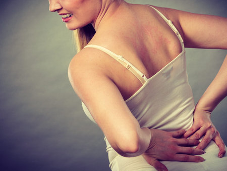 Long working hours and health. Young female with backache. Woman suffering from back pain on gray