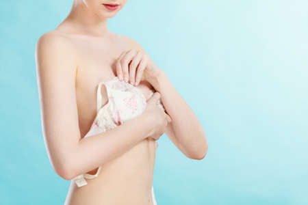 Bosom concept. Slim attractive naked woman dressing up or putting on her white lacy bra on blueの写真素材