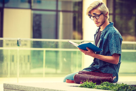Male fashion, student concept. Guy holding and studying from notebook wearing jeans outfit and...