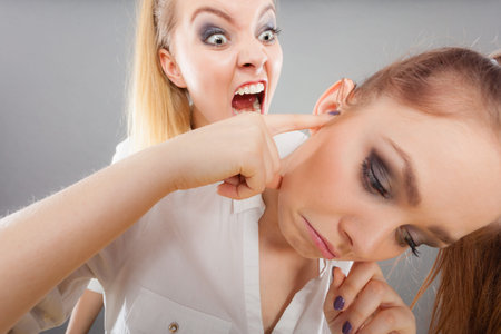 Conflict, bad relationships, friendship difficulties. Two young women having argument. Angry fury girl screaming at her friend or younger sister, female closing his ears, not listeningの写真素材
