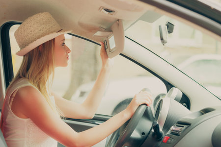 Distracted driver. Young attractive woman looking in mirror while driving the car.