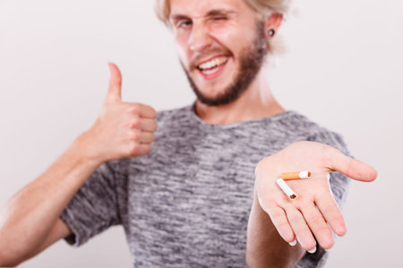 Successful guy showing broken cigarette making thumb up sign gesture. Winning with addicted nicotine...
