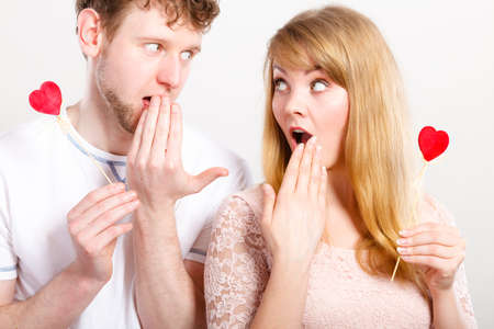 Surprise concept. Young lovers girlfriend boyfriend in big emotional shock. Female and male amazed holding little hearts on sticks.の写真素材