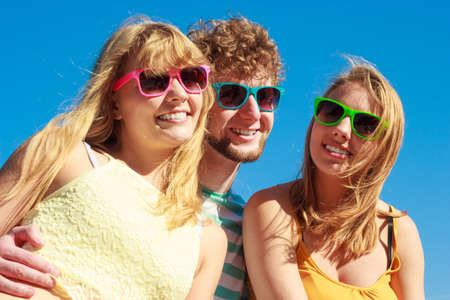 Friendship happiness summer holidays concept. Group of friends boy two girls in colorful sunglasses having fun outdoor against sky,  joy playful mood.の写真素材