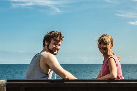 Couple man and woman dating by sea ocean outdoor. Young girl and guy sitting on bench. Summer love.の写真素材