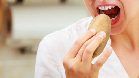 Closeup of woman eating raw potato food.の写真素材