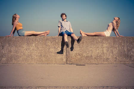 Happiness summer friendship concept. Group of friends spending time together having fun outdoor sitting on wall against blue skyの写真素材