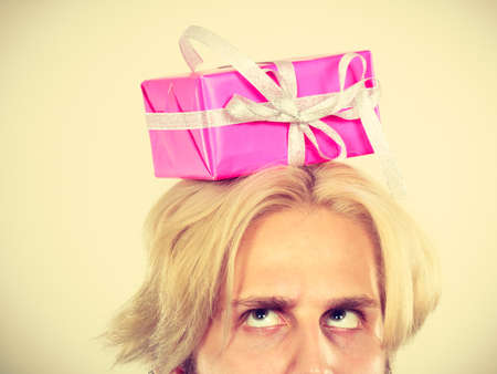 Celebration and giving concept. Cool young man with pink gift box on his head. Guy thinking looking for present ideaの写真素材
