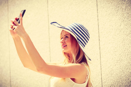 Technology, internet, social media concept. Young woman wearing sun hat taking picture of herself,...
