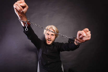 No freedom, social problems concept. Furious man with chained hands, studio shot on dark grunge backgroundの写真素材