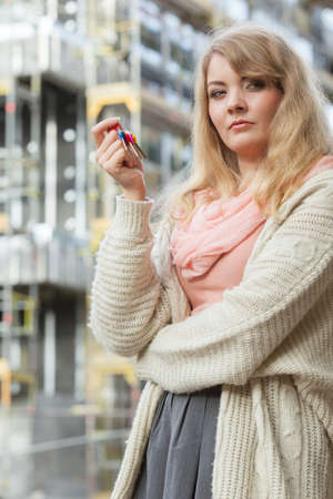 Real estate concept - young woman on front of new big modern house building construction site with keysの写真素材