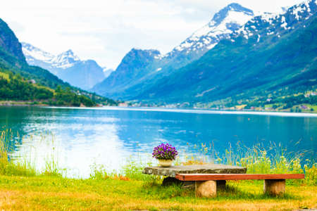 Tourism vacation and travel. Serene mountains landscape, rest place table with bunch of flowers on fjord shore, Olden village in Sogn og Fjordane county, Norway Europe.の写真素材