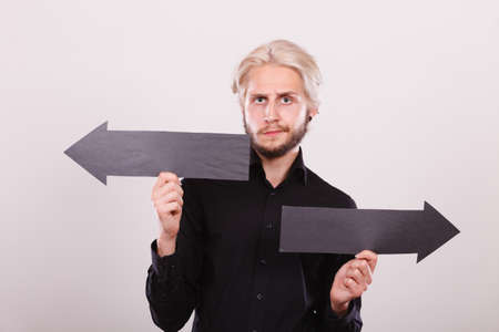 Planning, directions, choices concept. Man holding black arrow pointing left and right, opposite directions. Indoor shot on light backgroundの写真素材