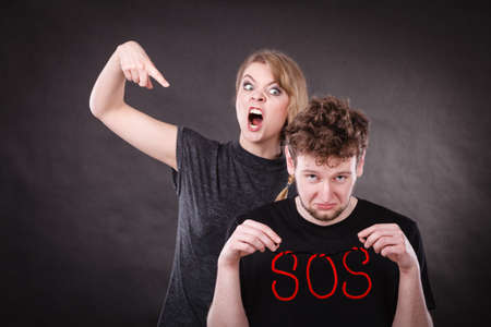 Betrayal and break up in relationship. Young couple arguing and holding red sos word sign symbol. Blonde woman in fury yelling on man. Negative emotions.の写真素材