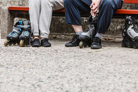 Closeup of people friends putting on roller skates outdoor. Woman and man sitting on bench.の写真素材