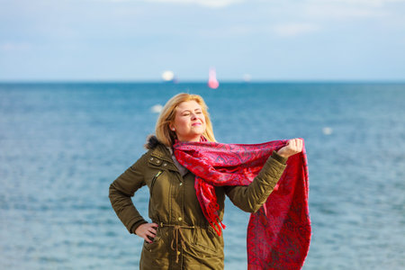 Happiness, enjoying weather, fashion concept. Woman wearing warm coat holding red beautiful scarf...
