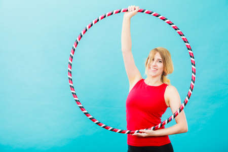 Fitness, activity, healthy lifestyle. Young blond woman doing exercise with hoop, on blueの写真素材