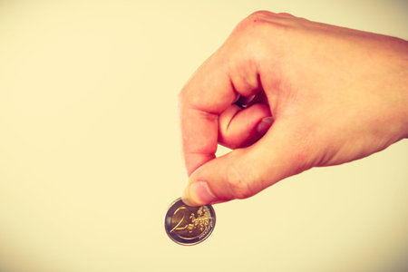 Savings and finances, economy concept. Holding money coin 2 eur, studio shot on light background