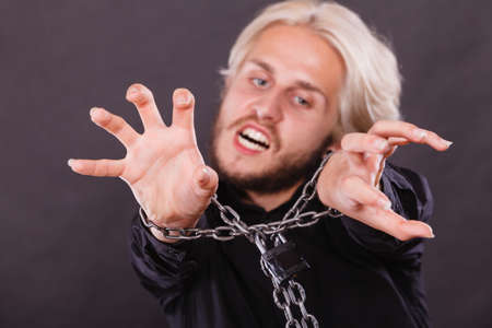 No freedom, social problems, human rights concept. Screaming furiously man with chained hands, studio shot on dark grunge backgroundの写真素材