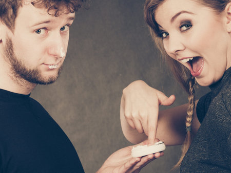 Protection and skincare. Stubborn girlfriend trying to apply cream on her boyfriend face. Man in...