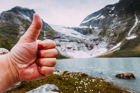 Man hand showing like with thumb up gesture on background of snowy mountains with glacier, approval and travel conceptの写真素材