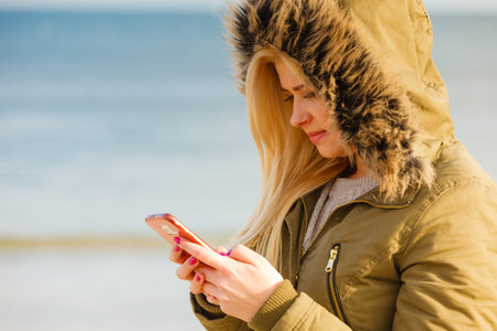 Social media, technology, modern devices, internet concept. Woman teenager wearing warm coat using...