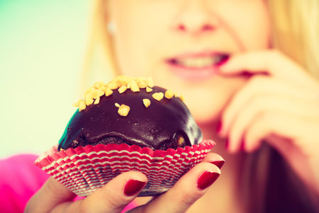 Diet, sweets, food concept. Cute blonde attractive woman thinking about eating delicious chocolate cupcakeの写真素材