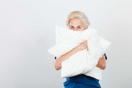 Man hiding her face behind pillow, studio shot on grayの写真素材
