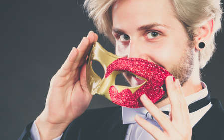 Holidays, people and celebration concept. Elegant young guy wearing suit white shirt bow tie and carnival venetian mask, on dark.の写真素材