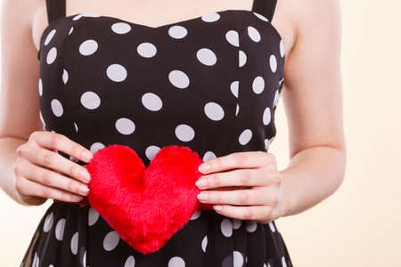 Valentine day gift, proof of love, romantic present concept. Woman in retro polka dot dress holding small furry red heartの写真素材