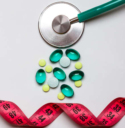 Healthy eating, medicine, health care, food supplements and weight loss concept. Pills with measuring tape and stethoscope on tableの写真素材