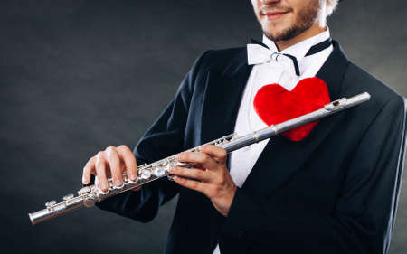 Valentines day love melody concept. Flute music playing male flutist musician performer. Young elegant stylish guy with instrument and red heartの写真素材