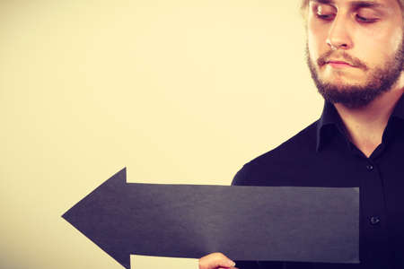 Planning, directions, choices concept. Man holding black arrow pointing left. Indoor shot on light backgroundの写真素材