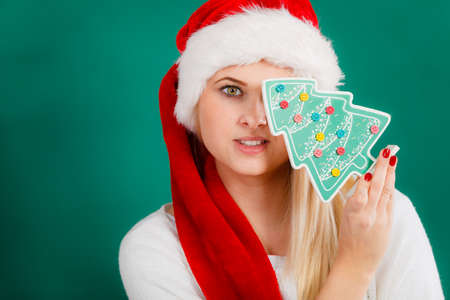 Enjoying cozy holiday interior, seasonal accessories concept. Blonde young woman in Santa hat holding little decorative Christmas tree.の写真素材
