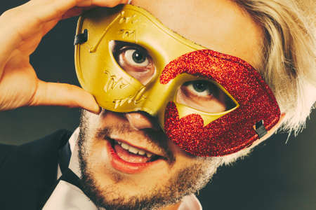 Holidays, people and celebration concept. Young guy wearing carnival venetian mask, on dark.の写真素材