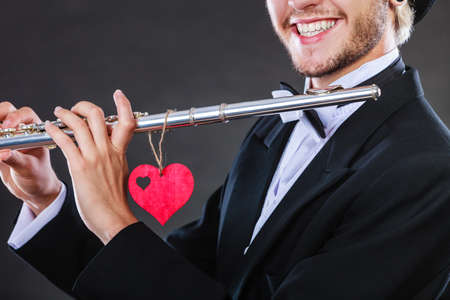 Valentines day love melody concept. Flute music playing male flutist musician performer. Young elegant stylish guy with instrument and red heartの写真素材