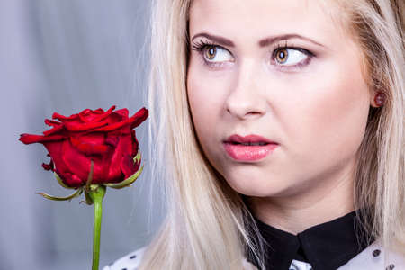 Romance, valentine day gifts concept. Beautiful blonde woman holding red rose looking melancholicの写真素材