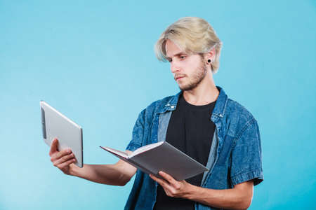 Male student holding ebook reader and book. Choice between modern educational technology and traditional way method. Young guy with digital tablet pc and textbook.の写真素材