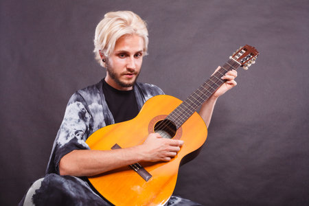 Music, passion concept. Young blonde man wearing fancy shirt playing on acoustic guitar, studio...