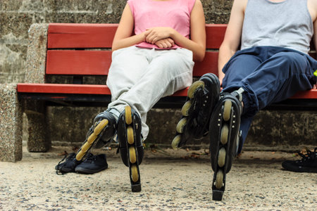 People friends in training suit with roller skates. Woman and man relaxing on bench outdoor.
