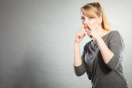Filth hygiene gross garbage smell concept. Blonde girl holding nose. Young lady pinching showing disgust smelling odor.の写真素材