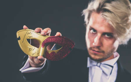 Holidays, people and celebration concept. Elegant young guy wearing suit white shirt bow tie and carnival venetian mask, on dark.の写真素材