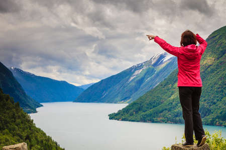 Travel concept. Tourist woman looking and pointing with finger at fjords beautiful mountains landscape in Norwayの写真素材