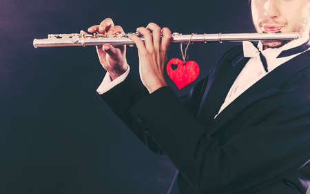 Valentines day love melody concept. Flute music playing male flutist musician performer. Young elegant stylish guy with instrument and red heartの写真素材