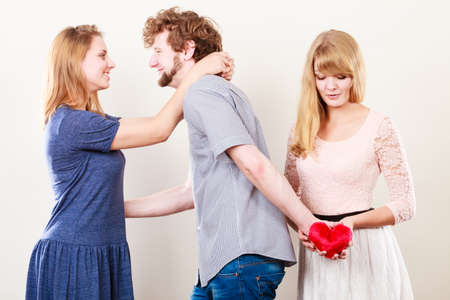 Betrayal and infidelity concept. Handsome boy with two attractive blondie girls. Man cheating women by mislead chosen one and offer his heart to another.の写真素材