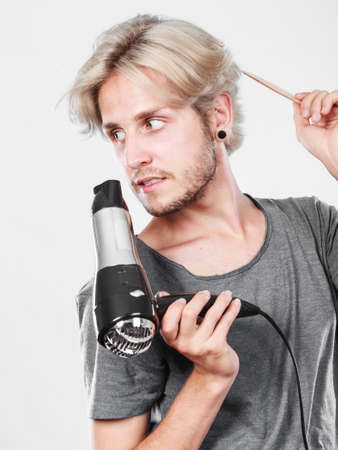 Hairstyle and fashion. Young trendy male hairstylist barber with new idea of look changing. Blonde man holding hair dryer and comb creating new hairdoの写真素材